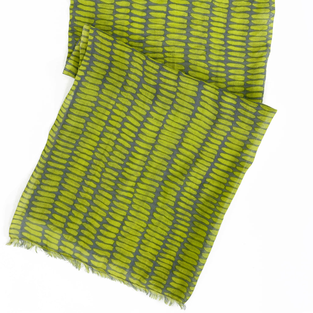 The See Design Wool Scarf, in green and gray with a repeating leaf pattern and slightly frayed edges, is shown laid flat on a white background.