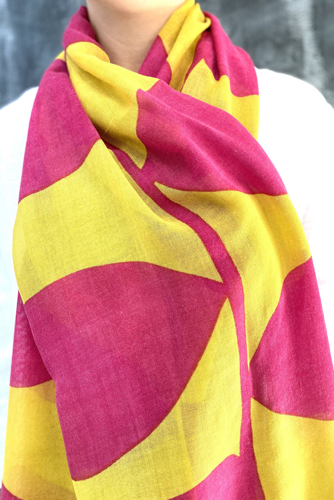 A woman wearing a bright yellow and pink See Design wool scarf.