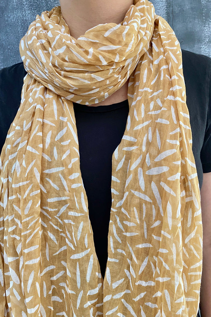 A woman wearing a bright yellow and white lightweight See Design cotton scarf with a luxurious touch.
