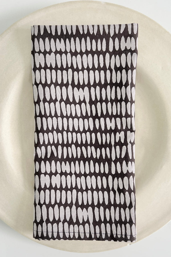 A vibrant, hand painted See Design black and white cotton napkin set of 4 on a plate.