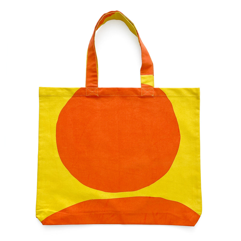 A lightweight, cotton canvas graphic tote bag with hand-painted artwork in orange and yellow by See Design.