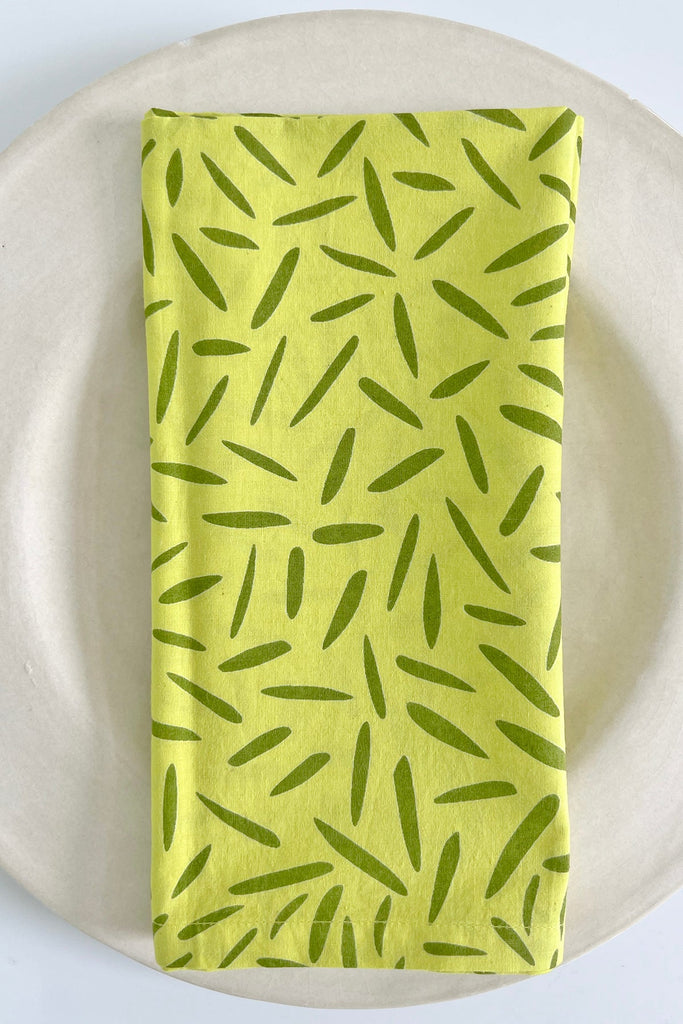 A set of 4 lime green cotton napkins by See Design on a white plate.