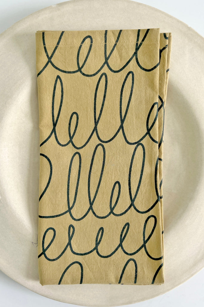 A colorful plate with a vibrant See Design cotton napkin set (set of 4) featuring a hand painted design of the word hello.