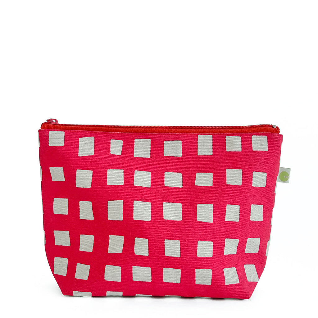A pink See Design Travel Pouch Large with white and grey squares on it.
