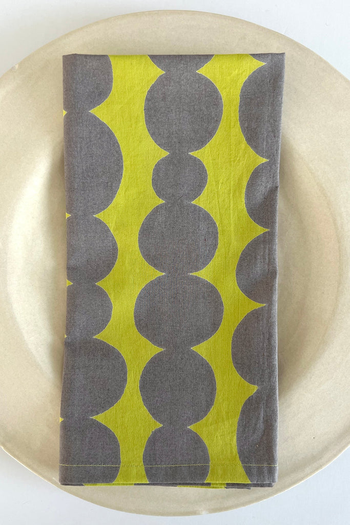 A vibrant yellow and grey cotton napkin (Set of 4) on a plate, See Design.