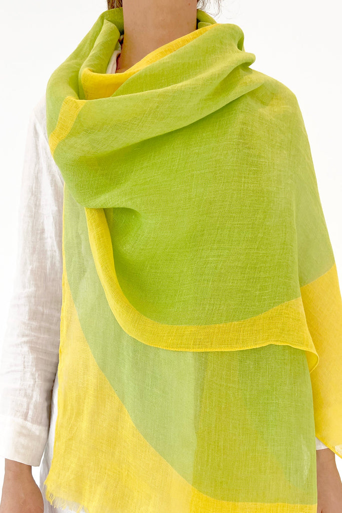 A woman donning a See Design linen scarf in vibrant green and yellow, showcasing colorful patterns inspired by modern design elements.