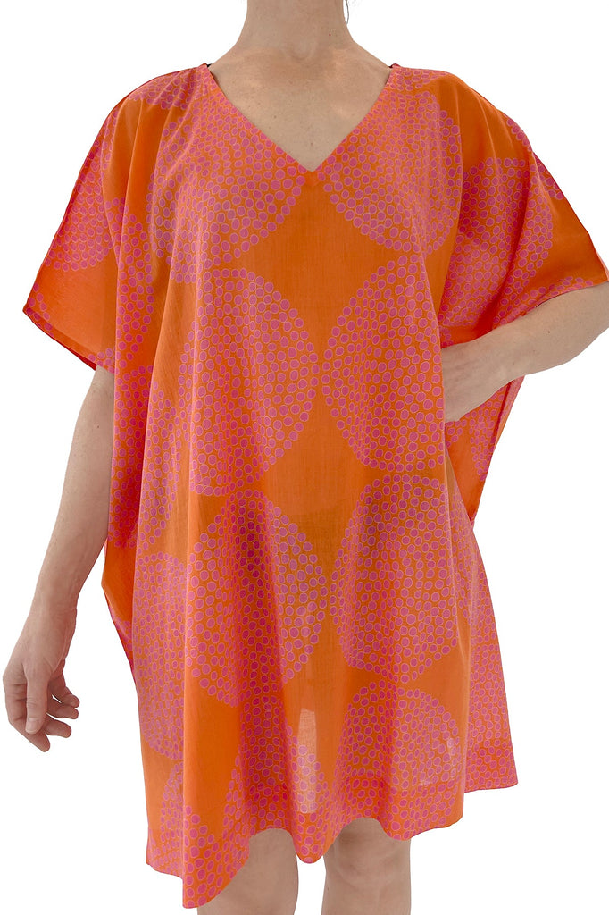 A lightweight woman wearing a cotton See Design caftan, beach-ready in orange and pink.