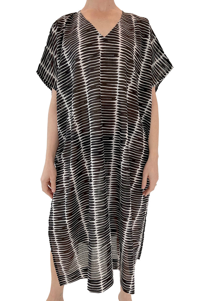A woman wearing a black and white striped cotton voile See Design Caftan Long, perfect as a lounge piece or beach cover up.