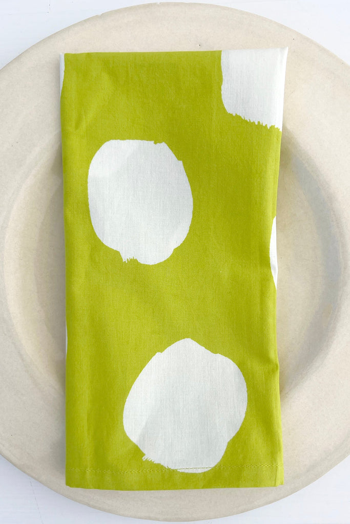 A plate with a See Design Lime and White Polka Dot Napkins (Set of 4) on a vibrant dinner table.