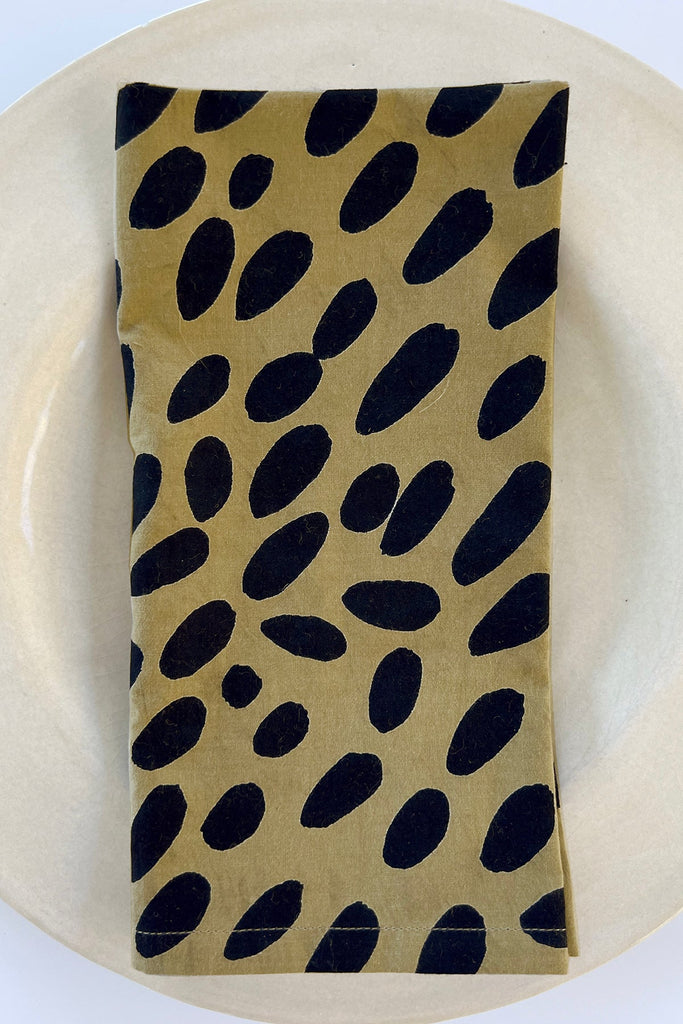 A See Design napkin (Set of 4) with gold and black spotted designs adorning a dinner table.