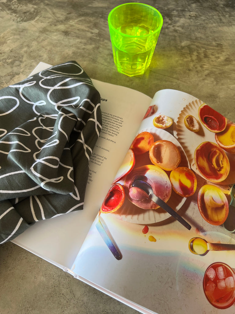 A colorful See Design Napkins (Set of 4) is open on a table next to a glass.