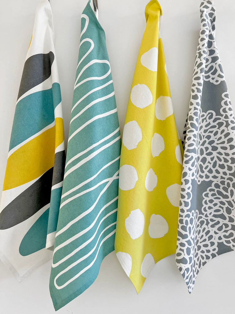Four See Design Tea Towels (Set of 2) hanging on a white wall.