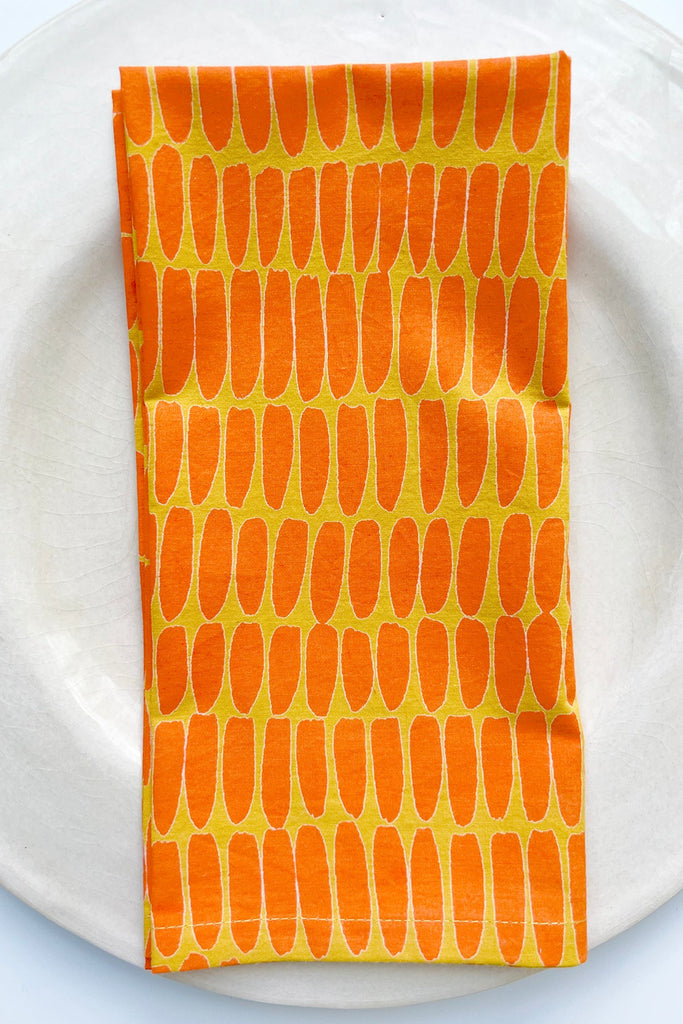 A See Design orange and yellow Napkins (Set of 4) on a plate with vibrant table linens.