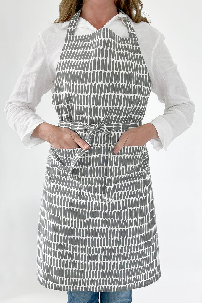A woman wearing a See Design kitchen apron with gray prints.