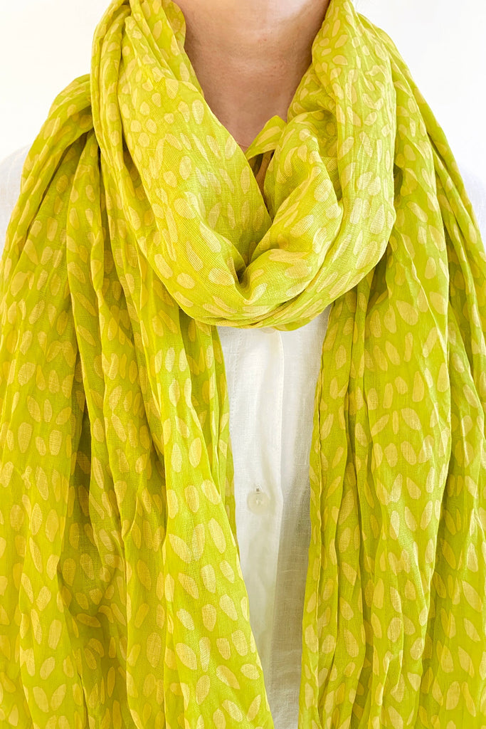 A woman wearing a See Design lightweight cotton scarf in green, adding a splash of color to her white shirt.