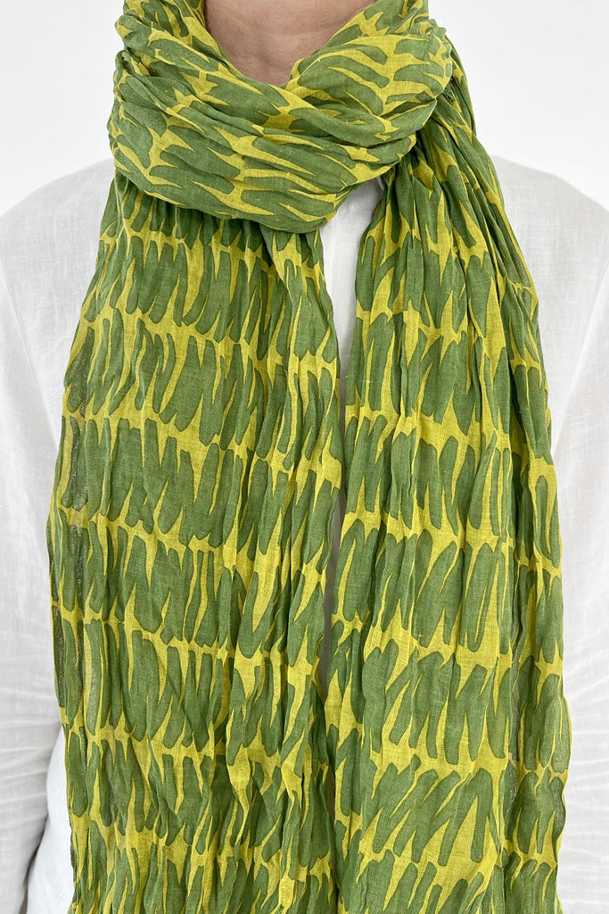 A woman wearing a lightweight green and yellow See Design cotton scarf.