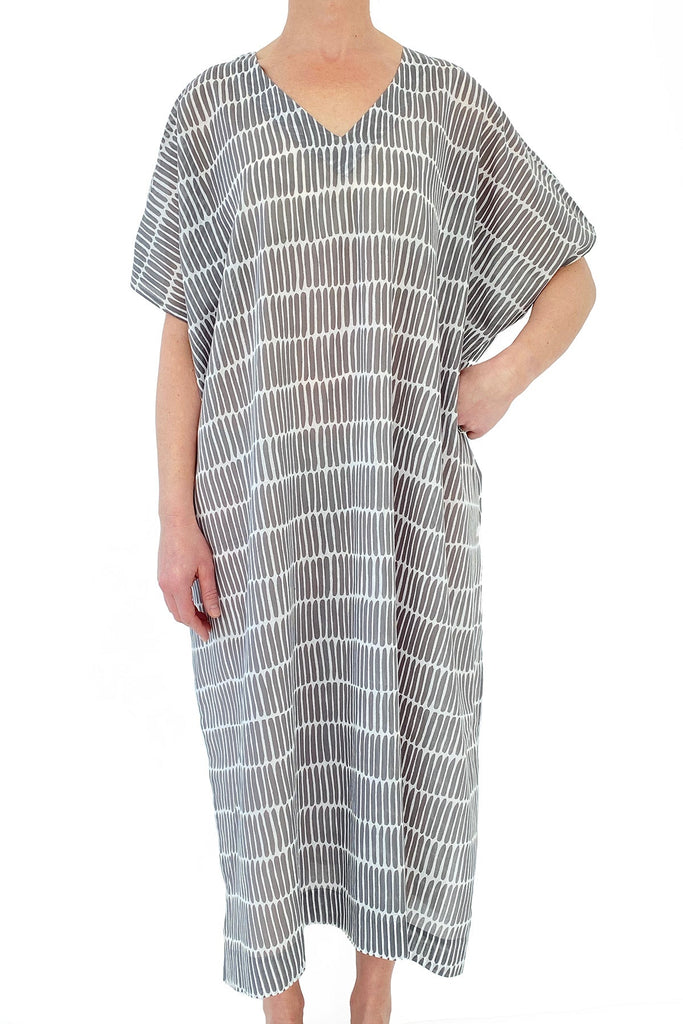 A woman wearing a beach cover-up, a Caftan Long by See Design, a grey and white striped kaftan dress.