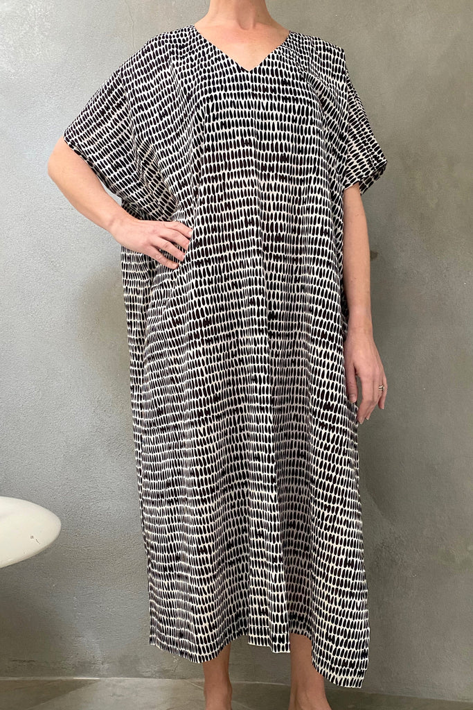 A woman wearing a flowing black and white patterned See Design Caftan Long, perfect as a lounge piece or beach cover up.