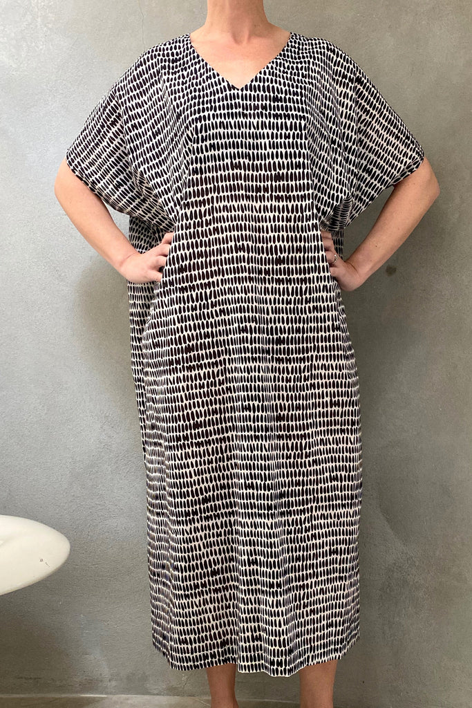 A woman in a black and white cotton voile Caftan Long dress, by See Design, standing in front of a toilet.
