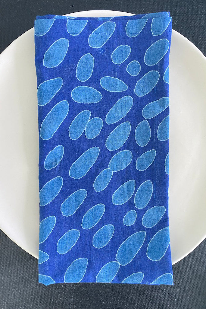 A set of 4 See Design cotton napkins with hand painted designs on a white dinner table plate.