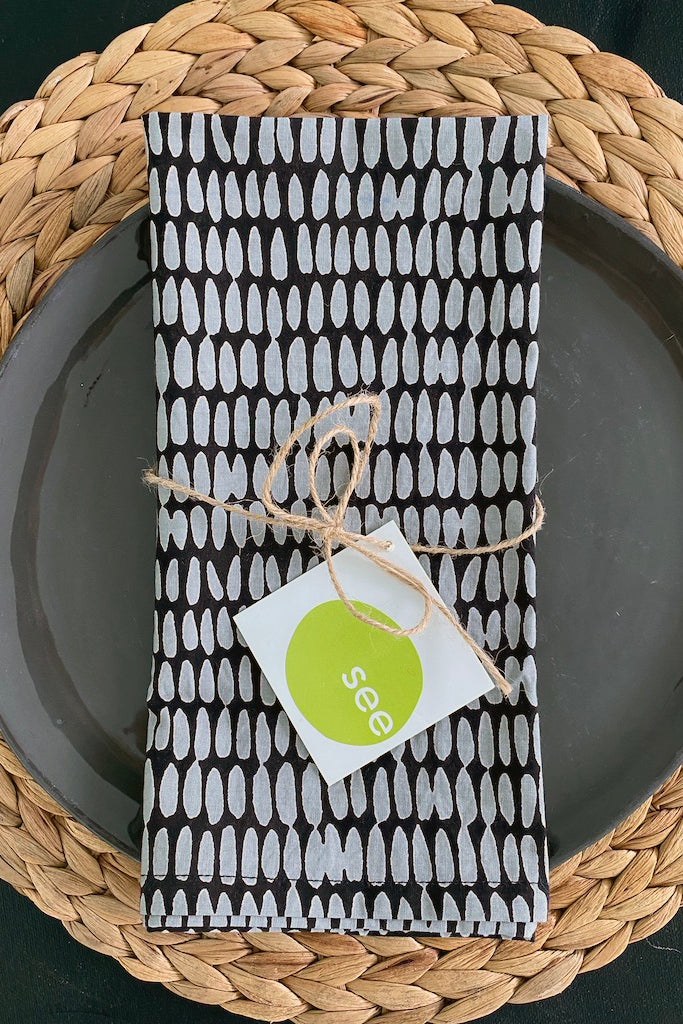 A hand painted design on a black and white See Design napkin (Set of 4) with a tag on it.