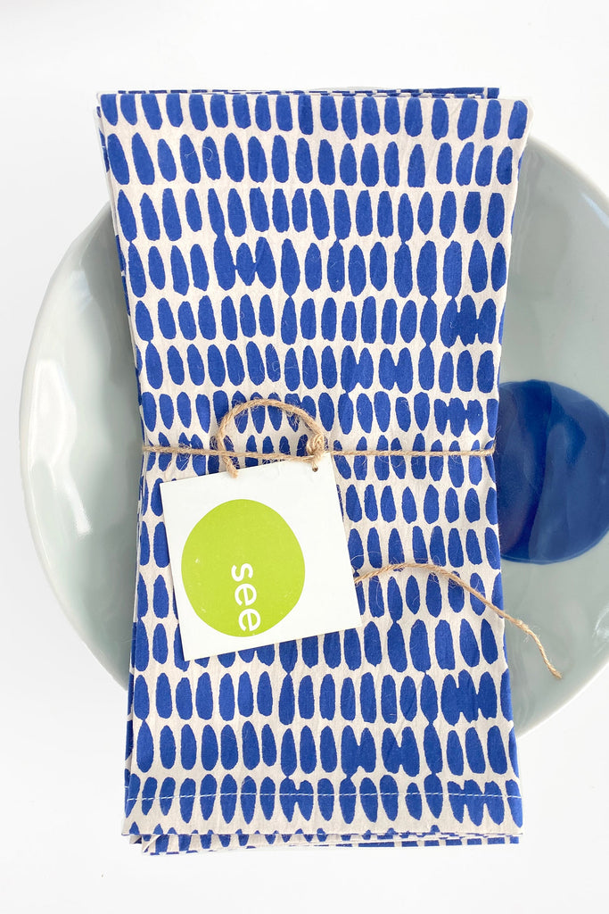 A vibrant, hand-painted See Design cotton napkin (Set of 4) with a tag on it.