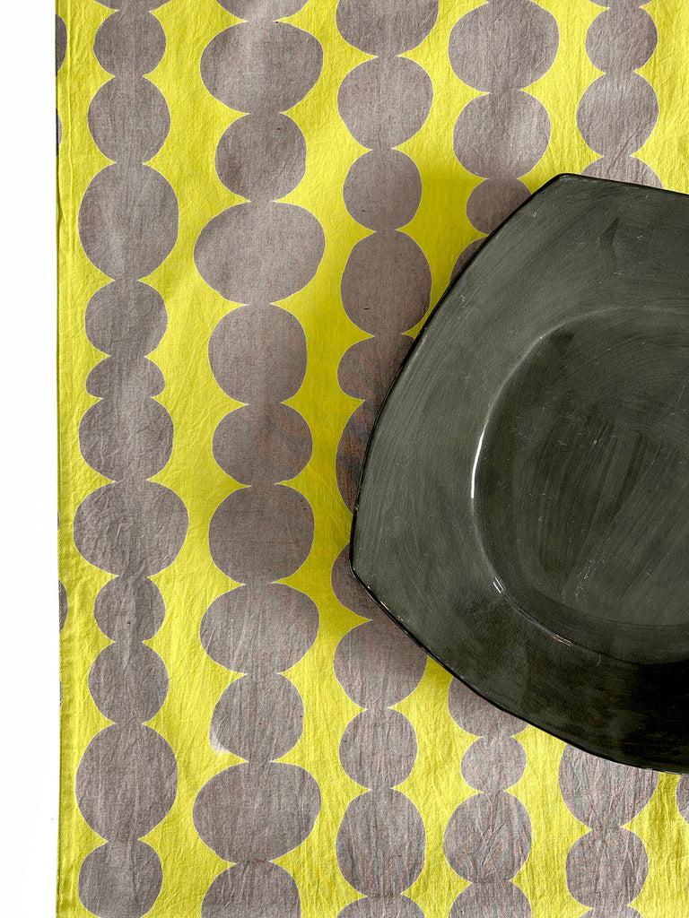 A vibrant yellow table runner with a sleek black plate on it, from See Design.