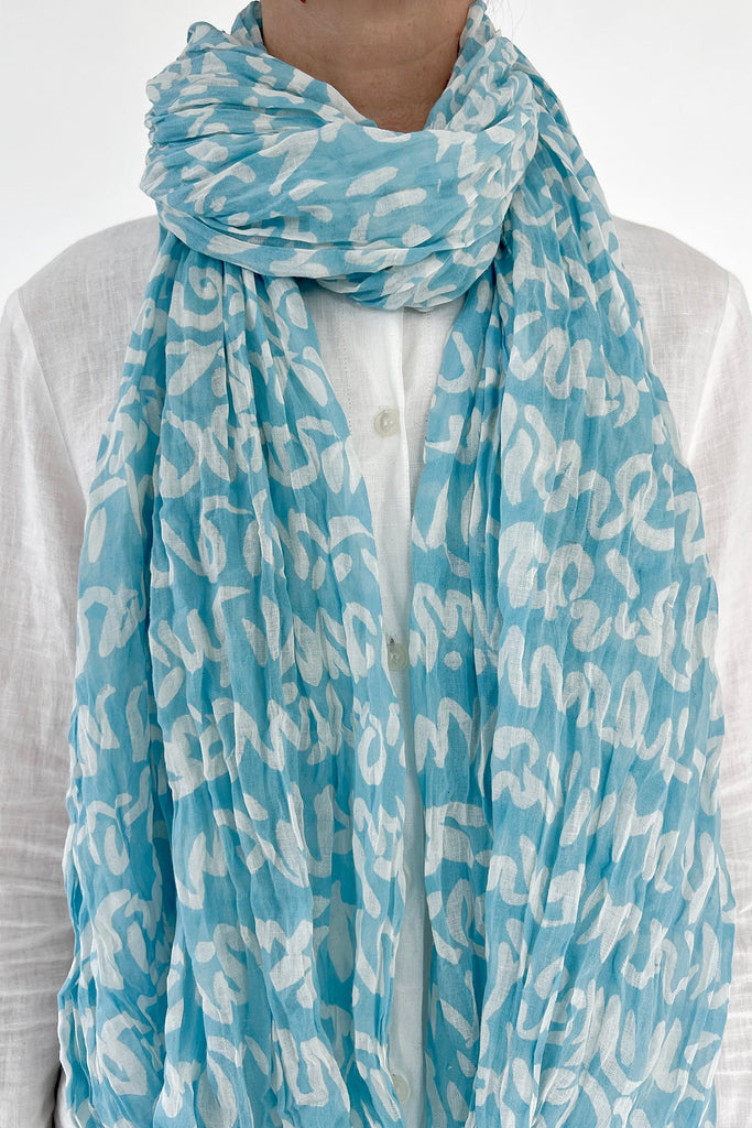 A woman wearing a lightweight blue and white See Design cotton scarf.