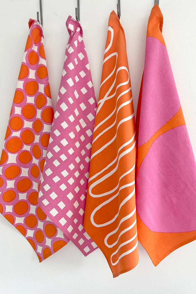 Four vibrant patterns of See Design hand painted Tea Towels (Set of 2), hanging on a hook.