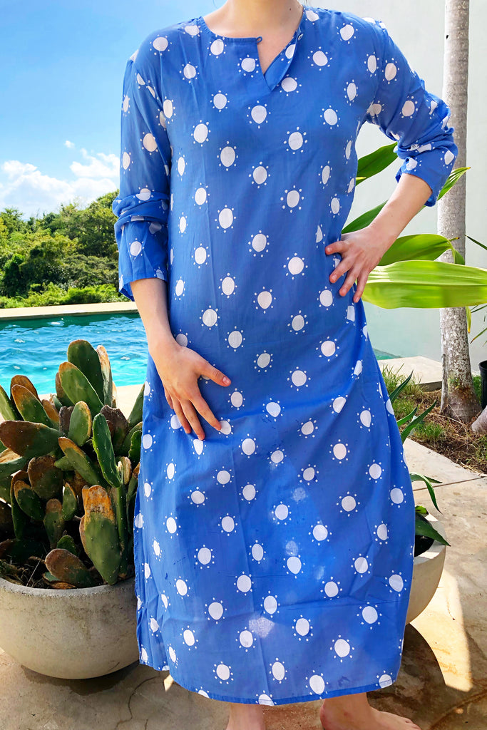 A woman wearing a blue and white polka dot See Design full length tunic dress made of lightweight and soft cotton voile.