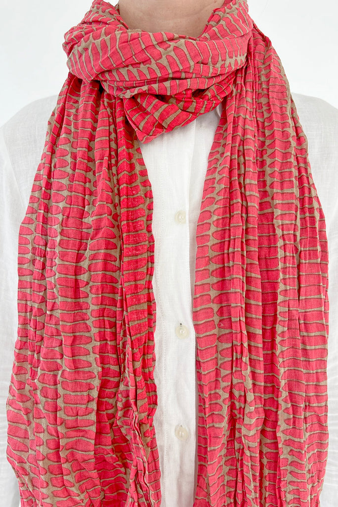The woman is wearing a See Design lightweight cotton scarf with a pink and green pattern.
